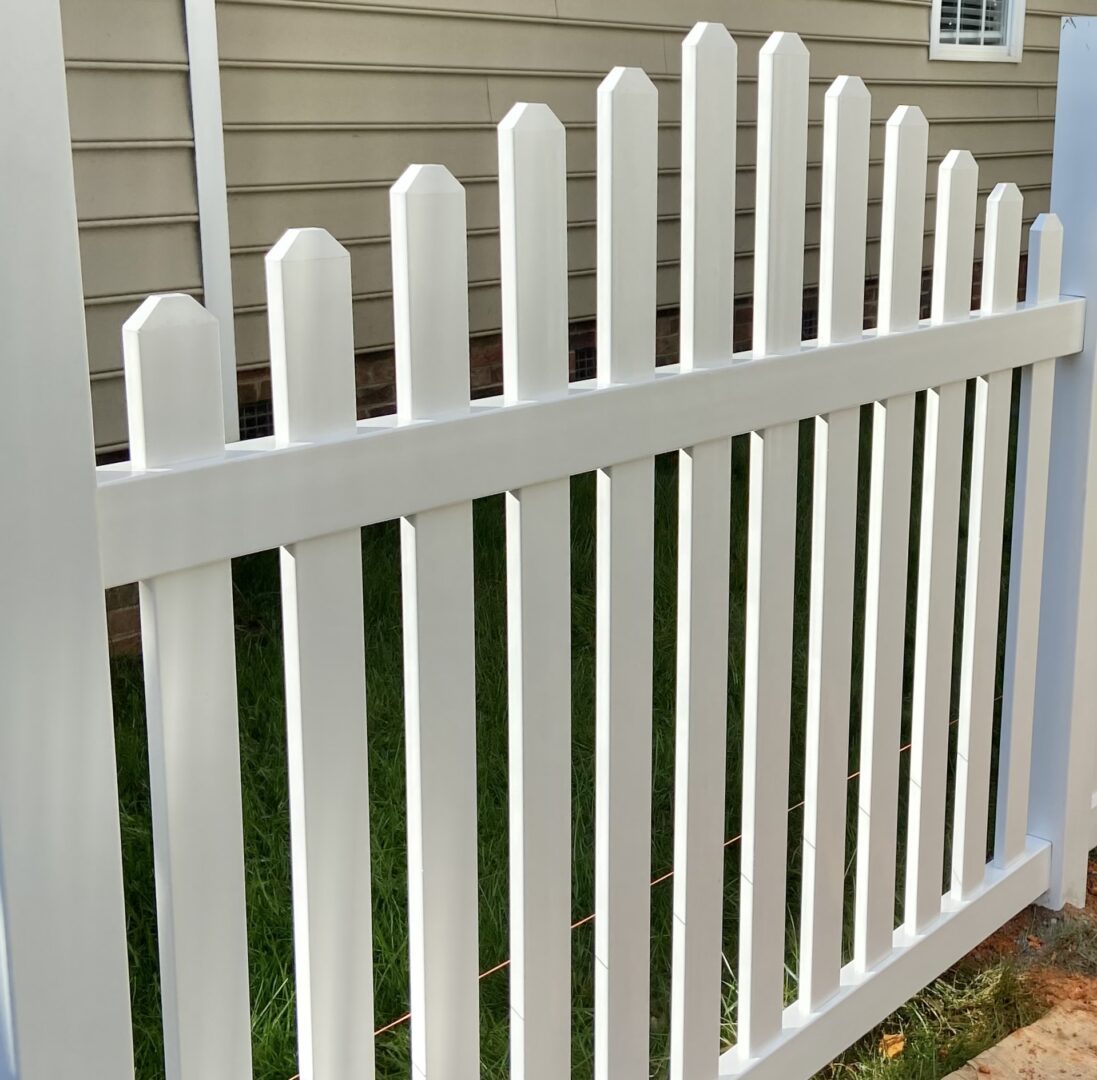 A white picket fence with grass growing around it.