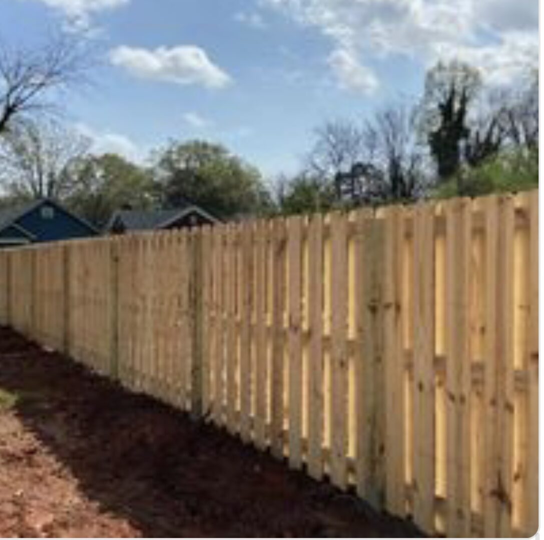 A wooden fence is shown with trees in the background.